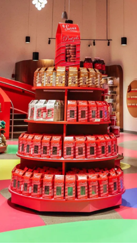 Sarris Candy Display | BAW Plastics Inc. | BAW Plastics Inc. Circular red display stand filled with red boxes of cookies or chocolates, arranged in multiple tiers in a bright store setting.