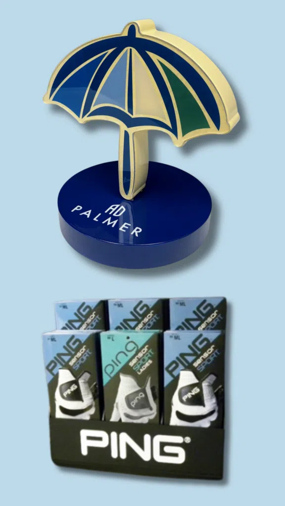 PING Display and AD Palmer Signage | BAW Plastics Inc. | BAW Plastics Inc. Enamel pin of a blue-and-gold umbrella on a blue base reading 'AD PALMER'; a row of Ping product packaging visible below.