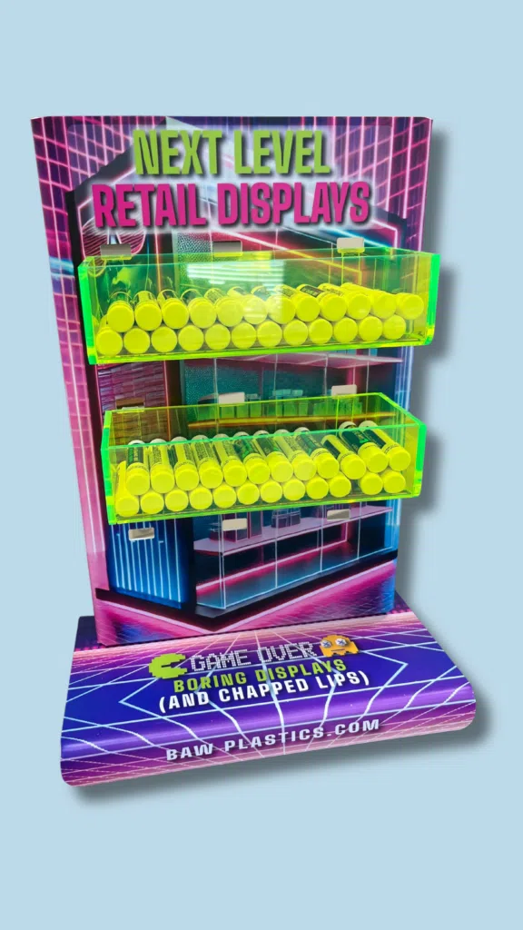 Next Level Retail Displays | BAW Plastics Inc. | BAW Plastics Inc. Retro arcade-style display with neon yellow capsules in clear shelves and a bold sign reading 'NEXT LEVEL RETAIL DISPLAYS'